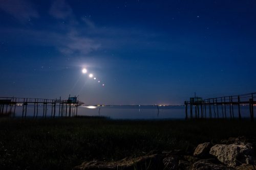Eclipse sur l’estuaire (Port Conac, 17) Le 16 mai 2022, une éclipse totale était visible depuis la France métropolitaine. Il y a deux éclipses lunaire par an, mais elles peuvent être partielles et ne s’observent que depuis un lieu précis, qui peut être n’importe où dans le monde. Hors là, toutes les conditions étaient réunies pour pouvoir faire cette image, au dessus des carrelets de l’estuaire. La lune est entièrement passée dans l’ombre de la Terre. La photo est un assemblage de différentes phases d’occultation de notre satellite : pleine lune, début de l’occultation, à moitié occultée, aux ¾, puis occultation complète. L’occultation complète est survenu proche de l’aube, ne permettant d’apprécier que les étoiles les plus brillantes dans le ciel.